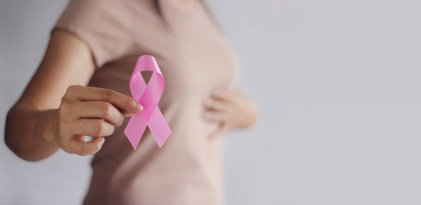 Woman holding a pink breast cancer awareness ribbon toward the camera, symbolizing support.