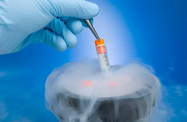 Gloved hand with tweezers placing a small test tube into a fog-filled container in a lab setting.