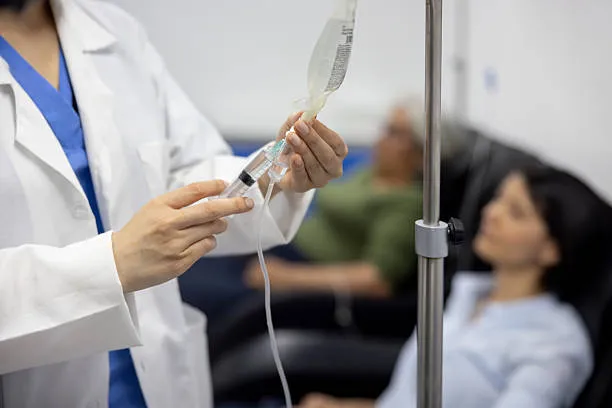 Healthcare professional prepares an IV drip for a patient, adjusting the IV bag and syringe in a clinical setting.
